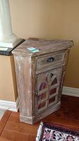Front view of the wooden corner stand showing a single drawer and a decorative mirrored door with a distressed finish.