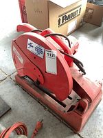 Side angle of the red Milwaukee 14 inch abrasive cut off machine showing the base, arm, handle, and power cord plugged in.