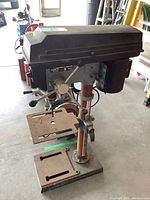 Side view of the Delta drill press showing rust on column, base, and table with the motor housing on top.