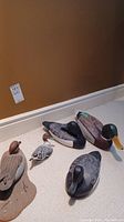 Group shot of five wooden duck decoys on floor against wall.