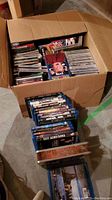 Full view of box filled with CDs and DVDs, and a line of Blu-ray DVD cases on floor.