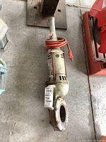 Full view of Rigid 700 electric pipe threader lying on concrete floor showing metal body, handle, and attached orange power cord with visible damage.