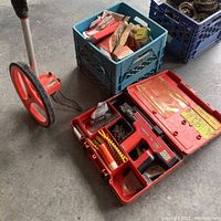 Full lot overview showing Hilti fastening tool case alongside measuring wheel and crates of fasteners/hardware.