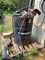 Full setup showing 45 gallon black metal fuel drum with Petro-Canada label on the side, rust visible on top. Fuel hose and nozzle attached, pump mounted on top.