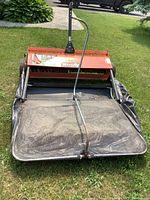 Front view of lawn sweeper with hopper, brushes, and collector bag attached on grass.