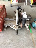 Front view of Delta Sidekick mitre saw showing blade, base and power cord, placed on floor with tags.