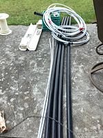 Photo showing black ABS pipes, white PEX pipe coils, and some plastic couplers all arranged on a concrete surface with grass in background.