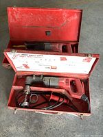Milwaukee red metal case holding heavy duty right angle corded drill with attached power cord and saw attachments
