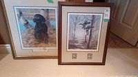 Framed wildlife prints showing a black Labrador puppy and flying wood ducks with framing and matting visible.