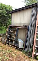 Four ladder‐style scaffold frames leaning against shed, blue and rusted finish