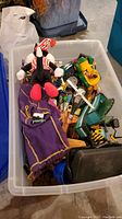 Photo showing assorted toys in a plastic bin including stuffed clown/jester and vehicle toys