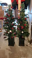 Two decorated artificial Christmas trees standing side by side in a basement setting.