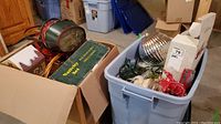 Photo showing multiple Christmas decoration items including storage bins (not included), a green and yellow boxed 10-piece ceramic Nativity set with real wood stable, a red fabric basket, metallic ornaments, and assorted string lights.