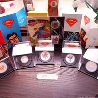 Overview of four silver coins in display capsules with original boxes and certificates of authenticity behind them.