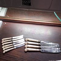 Set of 10 knives, 6 butter spreaders on left and 4 larger knives on right, displayed on dark wooden surface