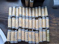 29 paper-wrapped rolls of U.S. nickels arranged on wooden surface, wrappers labeled “2 NICKELS 2” in blue with handwritten dates such as 1981