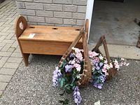 Photo of wood storage bench and two wooden hanging planters filled with faux pink and purple flowers sitting on a sidewalk.