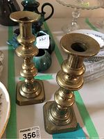 Pair of brass candlesticks standing upright, showing overall shape and aged patina.