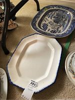 Two antique china serving platters; one rectangular with blue willow design and one plain white with a blue rim edge, both ceramic.