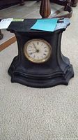 Full view of black iron mantel clock with curved sides and base showing overall shape and size.