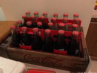 Top-down view of the wooden Coca-Cola case filled with 24 bottles showing red caps and classic logo labeling on bottles and crate sides.