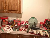 Overview photo showing collection of Coca-Cola branded items including tins, bottles, mugs, model trucks, linens, soap dispenser, tray, and floor mat