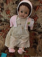 Front view of vintage baby doll sitting on patterned fabric sofa wearing its outfit showing composite head and clothing details