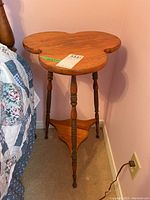 Side view of the solid wood cloverleaf occasional table next to bed and wall.