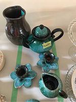 Overview of the pottery lot showing a dark brown jug, turquoise and black teapot with lid, two matching candlesticks and a turquoise small pitcher or creamer.