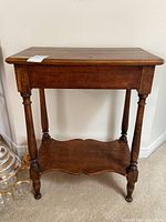 Front view of rustic wood side table showing rectangular top, turned legs, and lower shelf with scalloped edges.