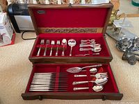 Overall view of the open wood canteen with red felt lining showing multiple flatware pieces including forks, knives, spoons, and serving utensils.