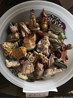 Top-down view of plastic tub containing around 50 small ceramic Wade tea figurines of various animals, humans and house shapes, some with visible chips.