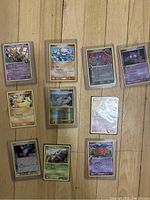 Photo showing all 10 Pokémon cards in sleeves laid out on floor, arranged in two rows of four and one row of two. Cards include a variety of characters and years from roughly 2000 to 2009.