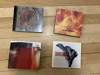 Four Nine Inch Nails CDs laid out on a wooden floor.