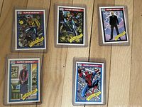 Front of 5 Marvel Super Heroes cards (Power Man, Longshot, Professor X, Aunt May, Spider-Man) each in hard plastic sleeves on wooden surface.