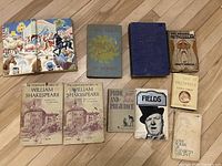 Top-down photo showing all 10 antique books arranged on a wooden floor. Titles include William Shakespeare Complete Works Vol 1 and 2, The Age of Heroes, Pride and Prejudice, Fields, The New World Museum, The Prophets by Agnes Smith, Love Poems by Elizabeth Sargent. Dust jackets and covers show signs of wear.