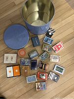 Blue metal tin with lid and multiple playing card decks laid outside the tin showing condition and variety.