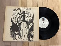Front cover of Planet Waves vinyl record showing abstract artwork in black and white with faces and album title.