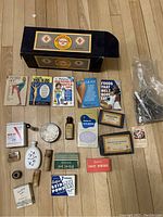 Full view of the vintage medical supplies arranged on wooden floor including original boxes, tins, glass bottles and vials, scissors, and manuals.