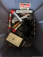 Photo showing various flashlights, metal scissors, a black travel case for playing cards, a white small box, and an Odor Remover packet all inside a plastic container.