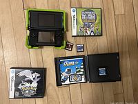 Nintendo DS console with green Nerf cover, four game cartridges and cases including Guinness World Records, Disney Club Penguin, and Pokemon Black case