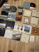 Photo showing an assortment of vintage audio tapes including reel-to-reel magnetic tapes, empty and full tape boxes from brands including Scotch, Radio Shack Concertape, and other boxes including some with handwritten labels.