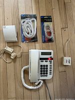 Full view of Nortel Vista 100 phone with coiled handset cord, power adapter, Nortel telephone adapter, and two packages containing coiled handset cord and phone cable all placed on a wooden floor.