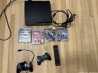 Full set image showing PS3 console with cables, two controllers, remote, and four game cases on floor