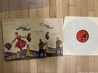 Front cover of The Sound of Music vinyl album showing artwork with characters jumping on a hillside, featuring Julie Andrews and other cast members.