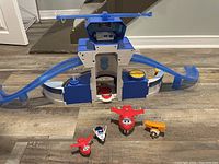 Blue and white Super Wings playset with ramps and four small airplane figurines in red, white, and yellow.