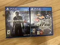 Photo of two PS4 game cases lying on a wooden surface: Uncharted 4: A Thief's End and The Crew