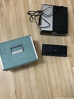 Two vintage projectors and a BOSS wireless system on a wooden floor, showing black and white/black projectors and carrying case