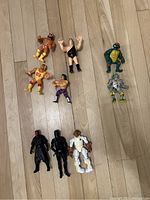 Nine vintage figurines arranged on a wooden floor: four WWF wrestlers with muscular builds and colorful costumes, two TMNT action figures, and three Star Wars robot/humanoid figures.