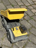 Photo of the vintage metal Tonka dump truck toy from a slightly elevated angle showing the yellow dump bed and gray cab with black smokestack, placed on outdoor pavement.